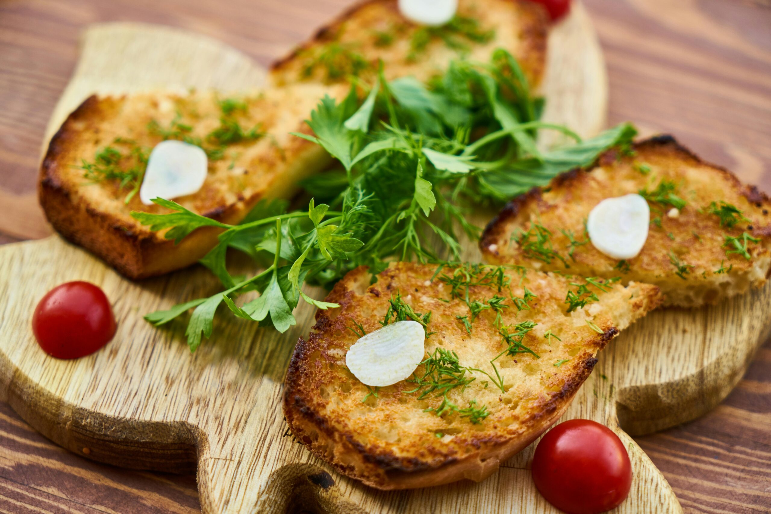 Freshly prepared garlic toast garnished with herbs and cherry tomatoes on a wooden board.