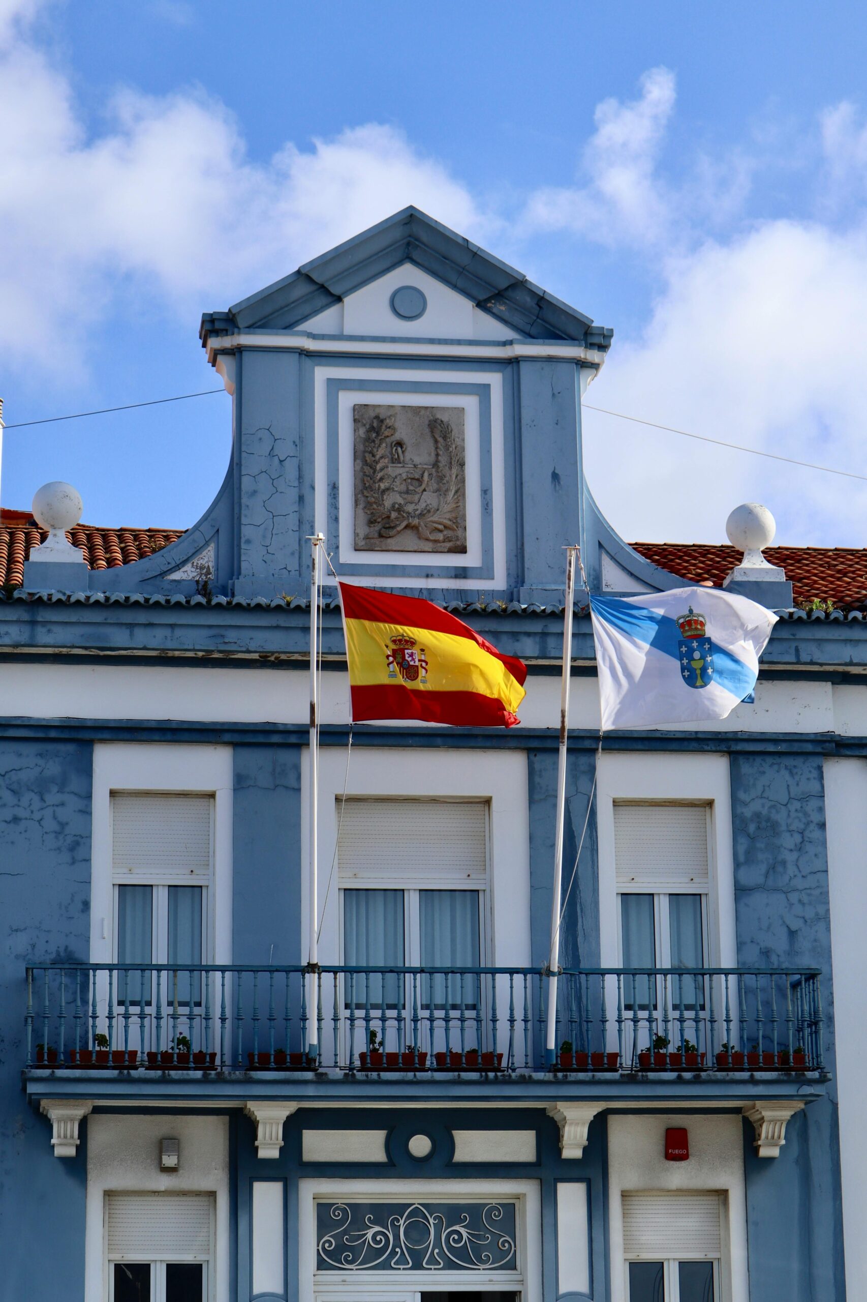 A historic building in Ferrol, Spain with Spanish and Galician flags displayed on the balcony.